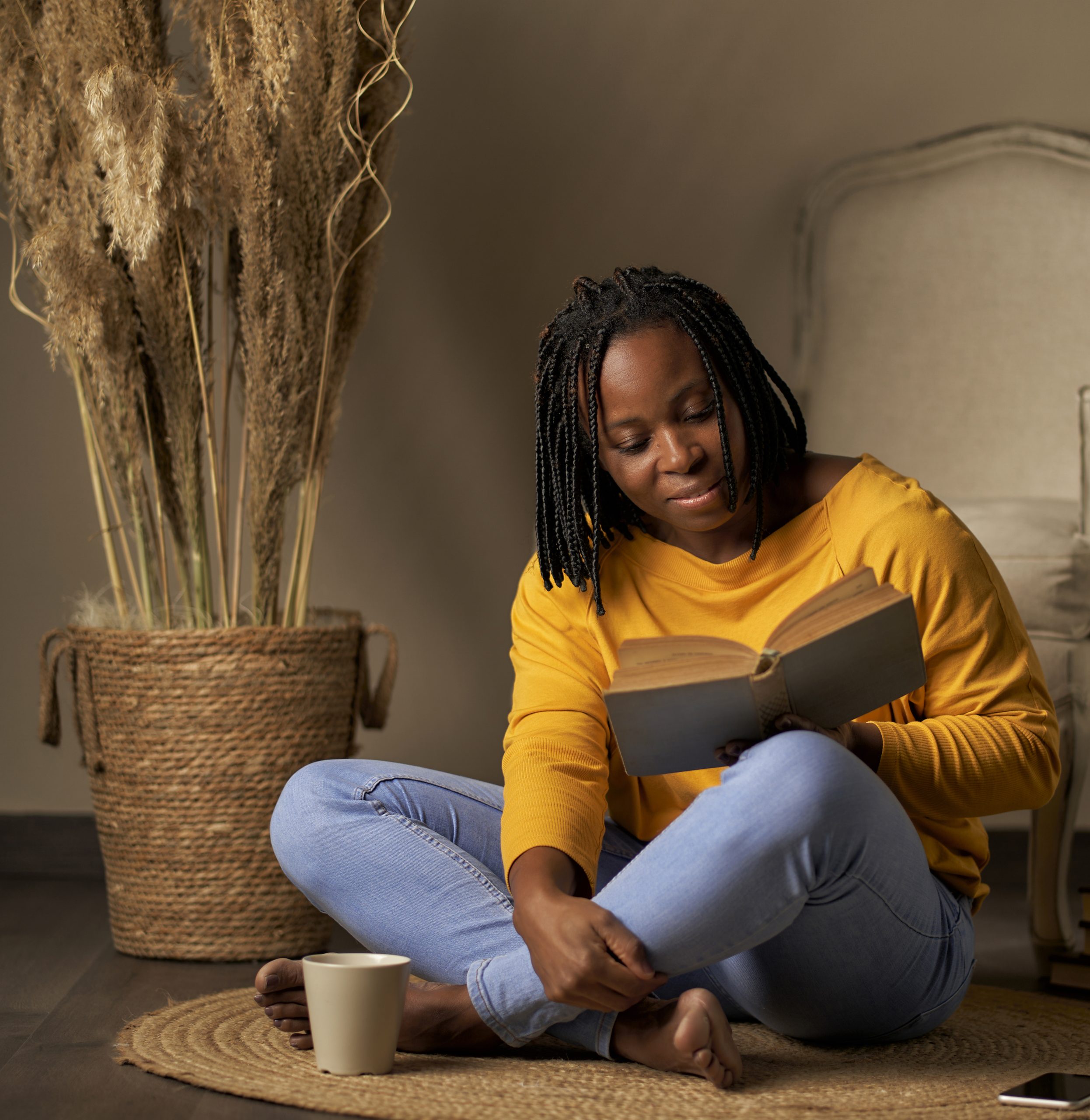 a black woman reading a book while sitting on a rug